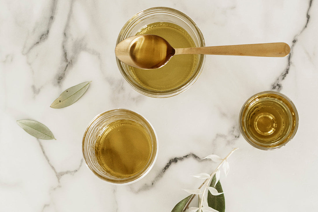 Bowls of golden olive oil with a spoon on a marble surface